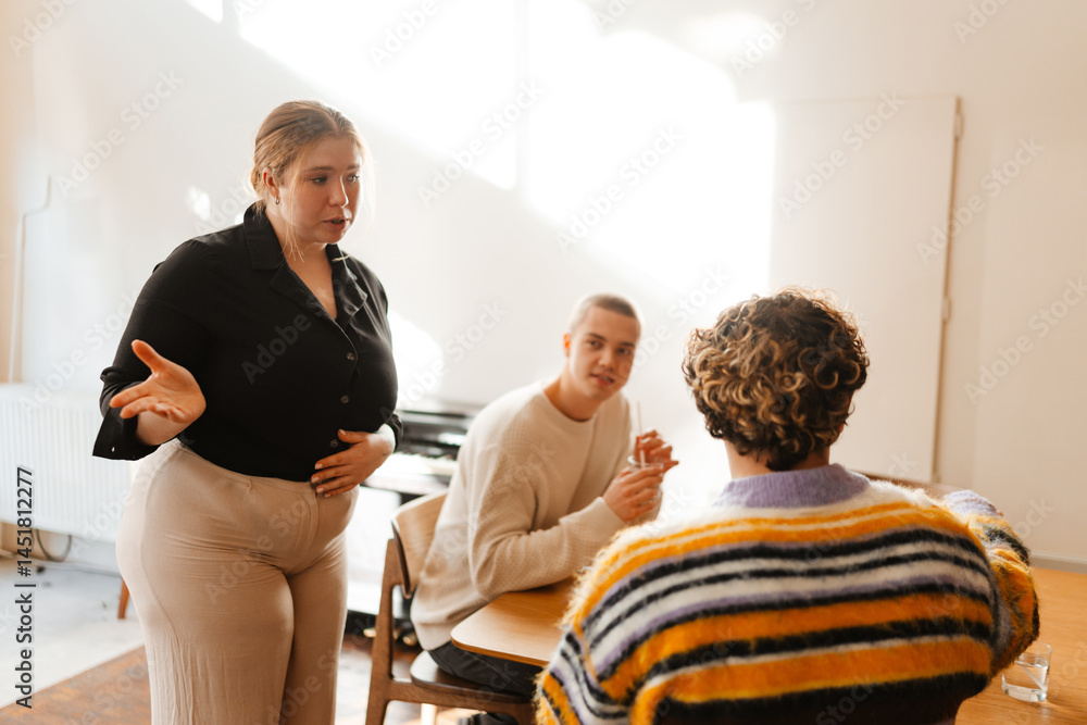 Fototapeta premium A serious dark-haired European female owner in her early 30s in a black shirt talking to a curly-haired adult man with white skin and a 20-year-old European male friend in a coffee shop.
