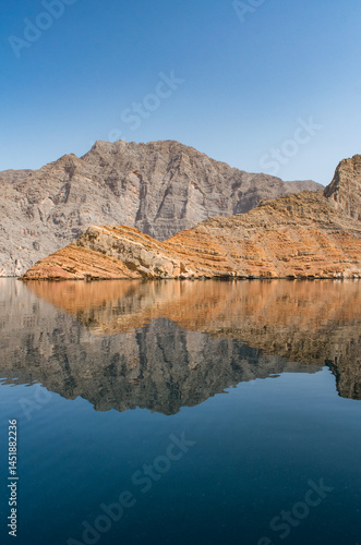 Oman, 03-06-2025: mountain reflection like in a mirror in the calm waters of the Strait of Hormuz cruising in the Musandam Peninsula, known as the Norway of Arabia for its unique desert fjords