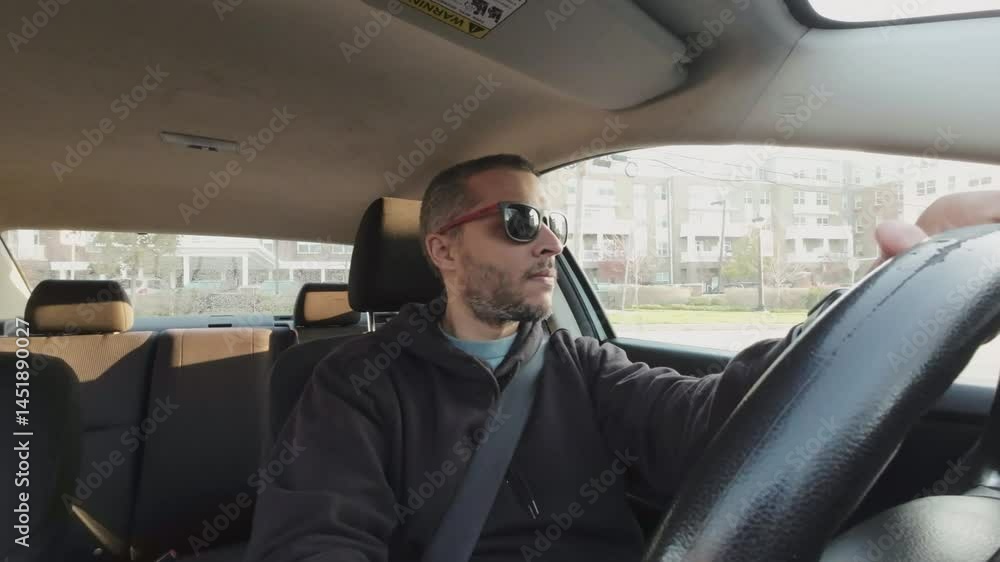 Male driver wearing sunglasses, navigating roadway with focused gaze while seated inside vehicle during daytime urban journey Male driver wearing sunglasses, navigating roadway with focused gaze while seated inside vehicle during daytime urban journey