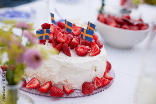 A close up of a table set with a cake of strawberries and whipped cream and a bowl of straberries in the background