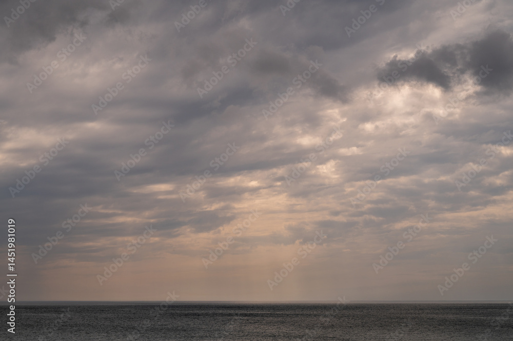 Sun between dark storm clouds over ocean. Dramatic seascape. Clouds and rain flurry over sea.