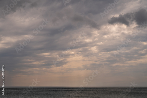 Obraz na płótnie Sun between dark storm clouds over ocean. Dramatic seascape. Clouds and rain flurry over sea. w salonie