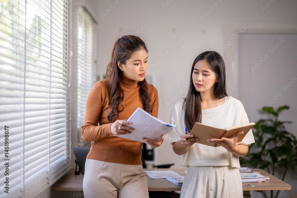 Two women are sitting at a desk, looking at papers Two women are sitting at a desk, looking at papers