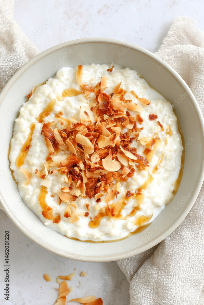 Creamy rice pudding topped with toasted coconut flakes and a drizzle of syrup in a gray bowl Creamy rice pudding topped with toasted coconut flakes and a drizzle of syrup in a gray bowl