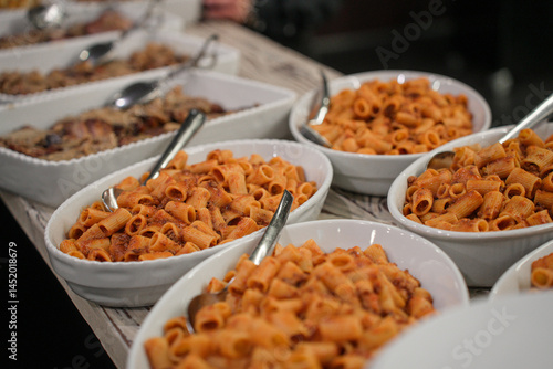 Detail of a restaurant buffet banquet with several trays of large portions of tomato pasta served for lunch