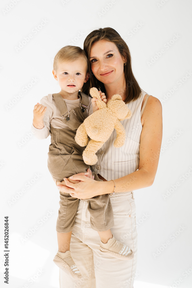 Young mother is holding a teddy bear while holding a son. Child is wearing a brown outfit