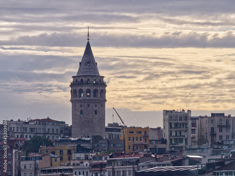 Fototapeta premium Historic Galata Tower rises above Istanbul's skyline at dusk, with cloudy sky and urban buildings