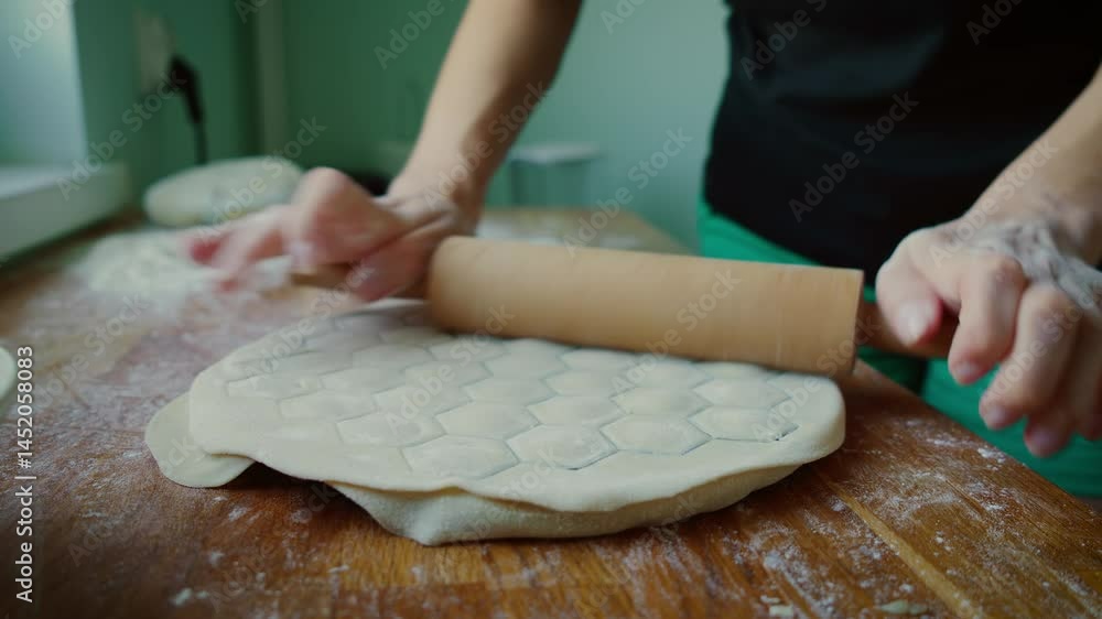 Hands rolling dough over dumpling mold with wooden rolling pin. Fingers pressing rolling pin to cut dumpling shapes in dough using mold. Hands creating dumpling outlines by rolling dough on textured Hands rolling dough over dumpling mold with wooden rolling pin. Fingers pressing rolling pin to cut dumpling shapes in dough using mold. Hands creating dumpling outlines by rolling dough on textured
