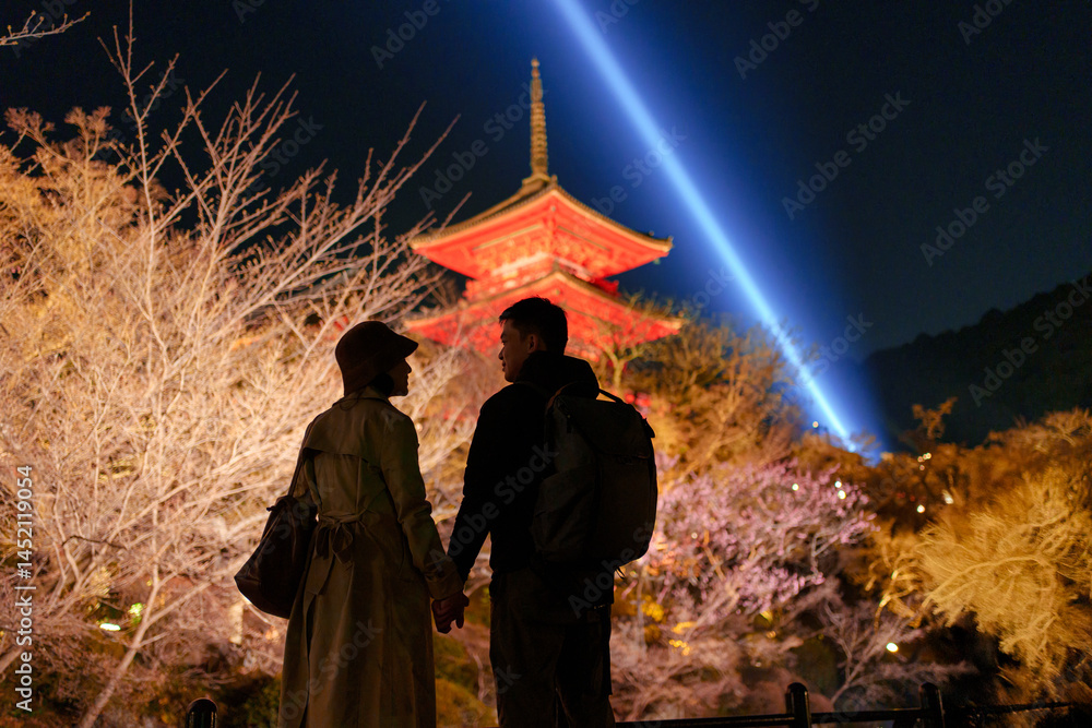 Fototapeta premium Asian couple shares a moment with illuminated pagoda and spotlight among spring garden at Kiyomizudera temple, Japan