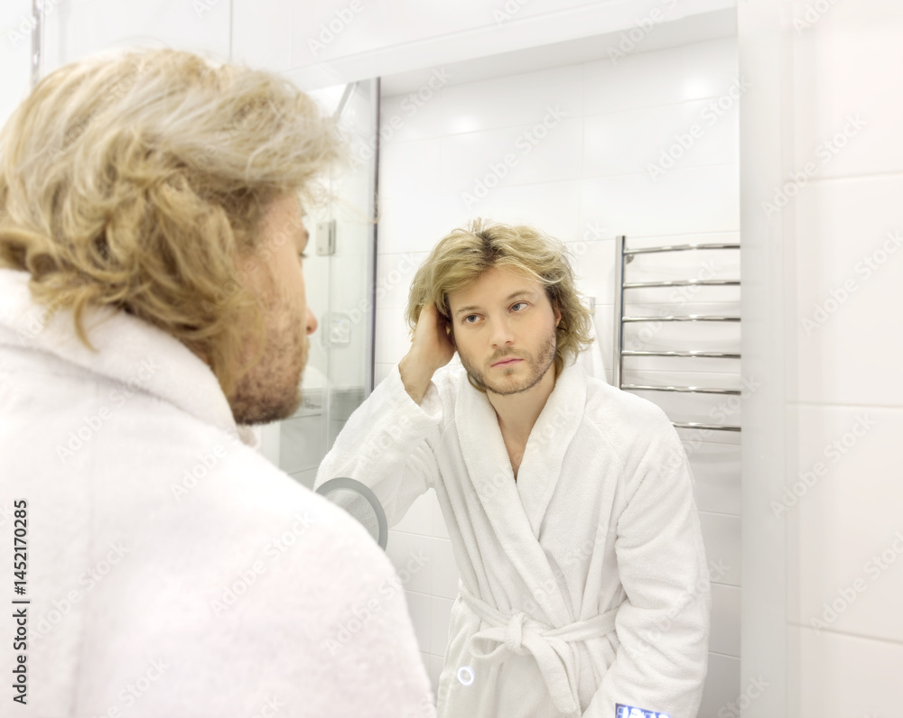Fototapeta premium morning routine, young man looking in mirror in bathroom