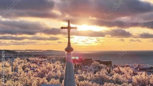 Wallpaper Mural Drone screen capture over Petoskey, Michigan’s ice storm aftermath during sunset: a church steeple cross dripping with icicles, silhouetted against fiery orange and purple skies, frozen townscape and  Torontodigital.ca