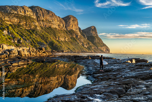 Photography A solo surfer prepares to enter the water - set against a beautiful mountain backdrop at dawn