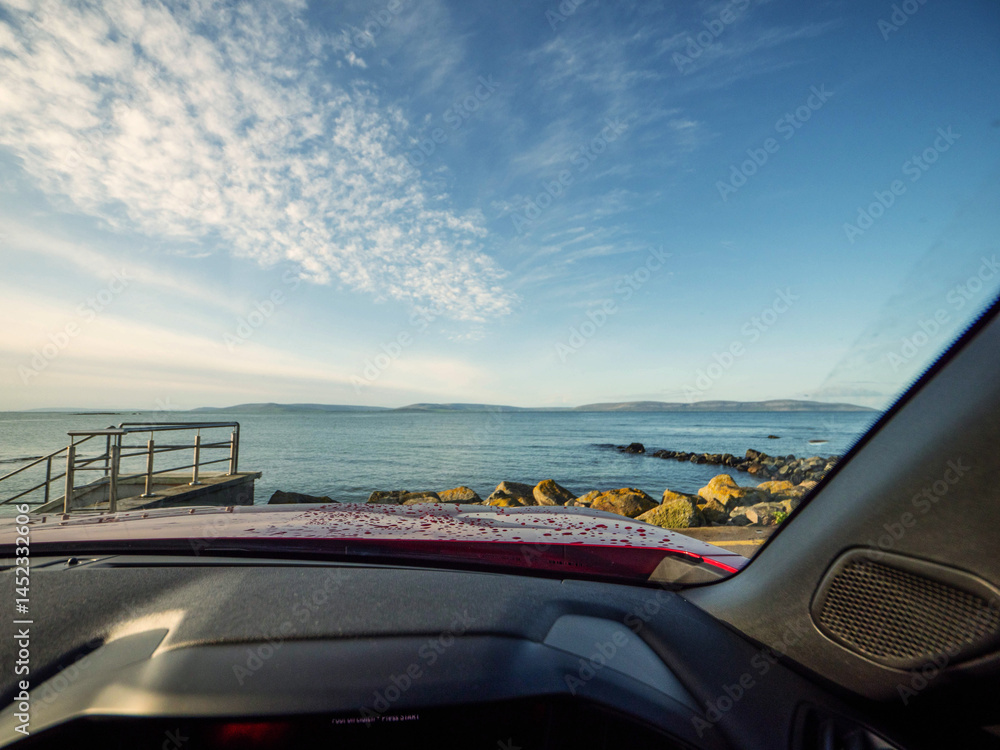View from a driver seat in a car on a Galway bay and Burren mountains and blue cloudy sky. Silverstrand area of Galway city. Travel and tourism. Rent car for trip concept. Landmark in Ireland.