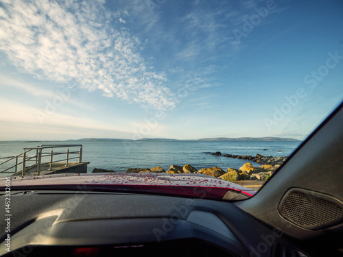 Obraz na płótnie View from a driver seat in a car on a Galway bay and Burren mountains and blue cloudy sky. Silverstrand area of Galway city. Travel and tourism. Rent car for trip concept. Landmark in Ireland. w salonie