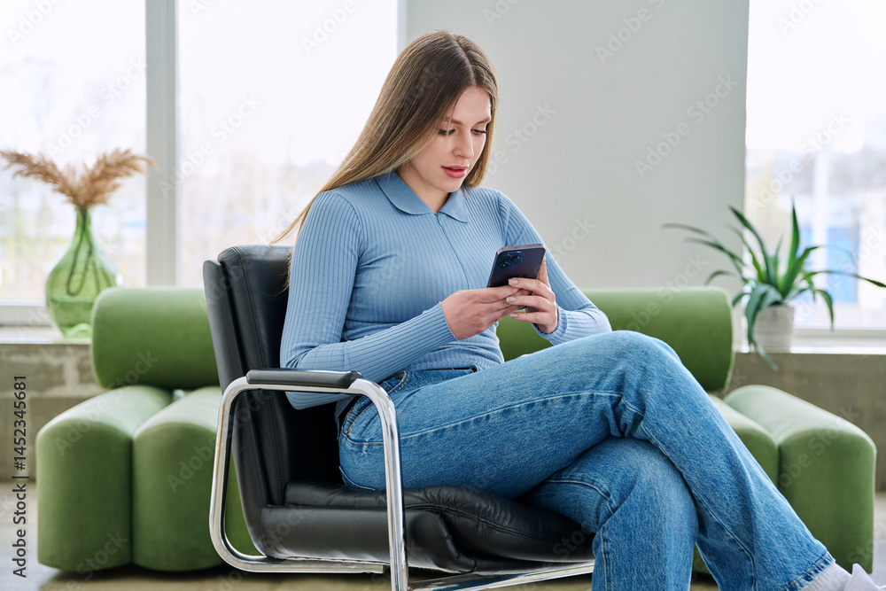 Young woman sitting at home in chair using smartphone