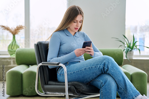 Obraz na płótnie Young woman sitting at home in chair using smartphone w salonie