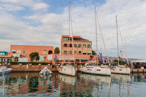 Portorosa port in Tonnarella city in Sicily. Sailing travel vacation. Sailing yachts and dinghy boats on the sea water surface under the blue sky. Marina with rosy buildings in Sicily, Aeolian Islands