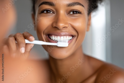 African woman smiles brightly brushing teeth in mirror, demonstrating dental hygiene with healthy gums and attractive white teeth.