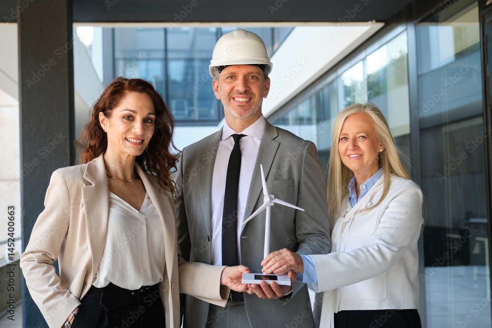 Group of engineers holding a model of a wind turbine and a solar panel, promoting clean energy solutions