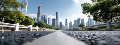 The bright day showcases an empty asphalt road winding alongside a river with lush greenery and a city skyline