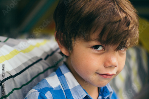 Close-up portrait of a smiling boy with brown hair sitting next to his bed