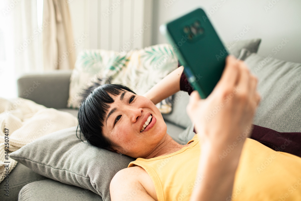 Smiling woman relaxing on couch having video call on smartphone Smiling woman relaxing on couch having video call on smartphone