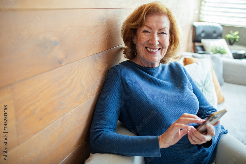 Senior woman smiling while using smartphone at home in bright living room