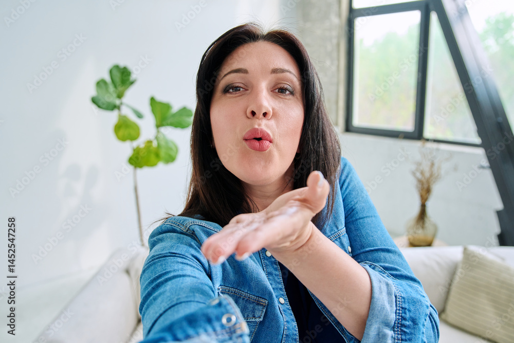 Selfie portrait happy beautiful woman blowing a kiss gesture in home interior