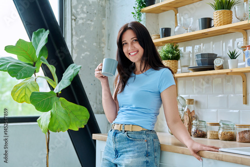 Portrait of beautiful smiling 30s woman with cup of coffee at home in kitchen