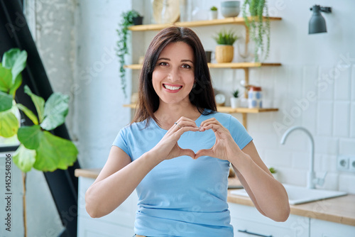 Obraz na płótnie Portrait young smiling woman making heart gesture with her hands at home w salonie