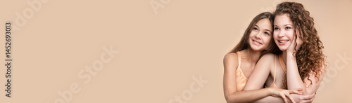 Obraz na płótnie Banner with studio portrait of two beautiful smiling sisters sitting together against beige background w salonie