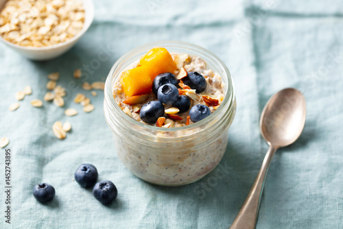Healthy breakfast. Overnight oats with fresh berries and fruits in glass jars. Blue textile background. Close up.