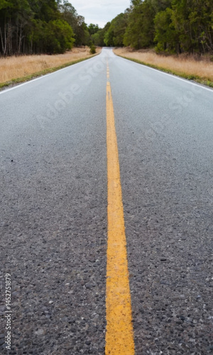 Obraz na płótnie A straight and empty road with a bright yellow centerline, suitable for traffic or infrastructure-related uses w salonie