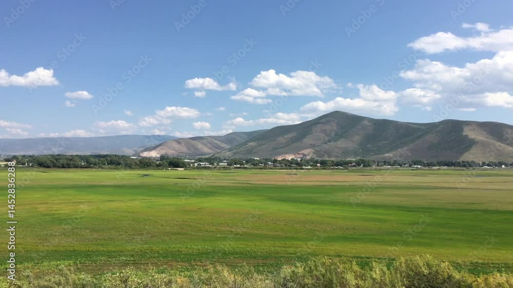 Handheld camera out of the window of a train passing through Heber Valley Utah. Lush green meadow and Wasatch Mountain Range, puffy clouds and blue sky. Passing through Heber Utah on a train. Handheld camera out of the window of a train passing through Heber Valley Utah. Lush green meadow and Wasatch Mountain Range, puffy clouds and blue sky. Passing through Heber Utah on a train.