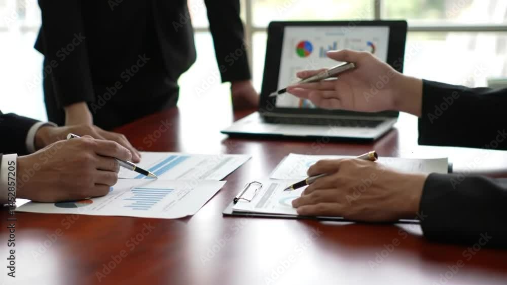 Business meeting with charts on laptop and documents on table in office setting Business meeting with charts on laptop and documents on table in office setting