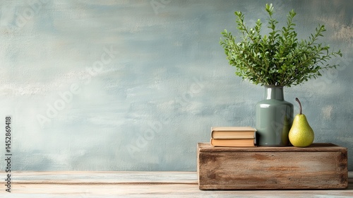 A serene tabletop display featuring a green vase with foliage, two books, and a pear, creating a harmonious and inviting atmosphere befitting modern home decor.