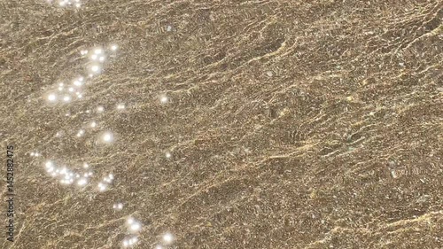 Close-up image of a sandy beach with gentle waves forming delicate patterns on the surface. Captures the serene natural textures and details of the shoreline.