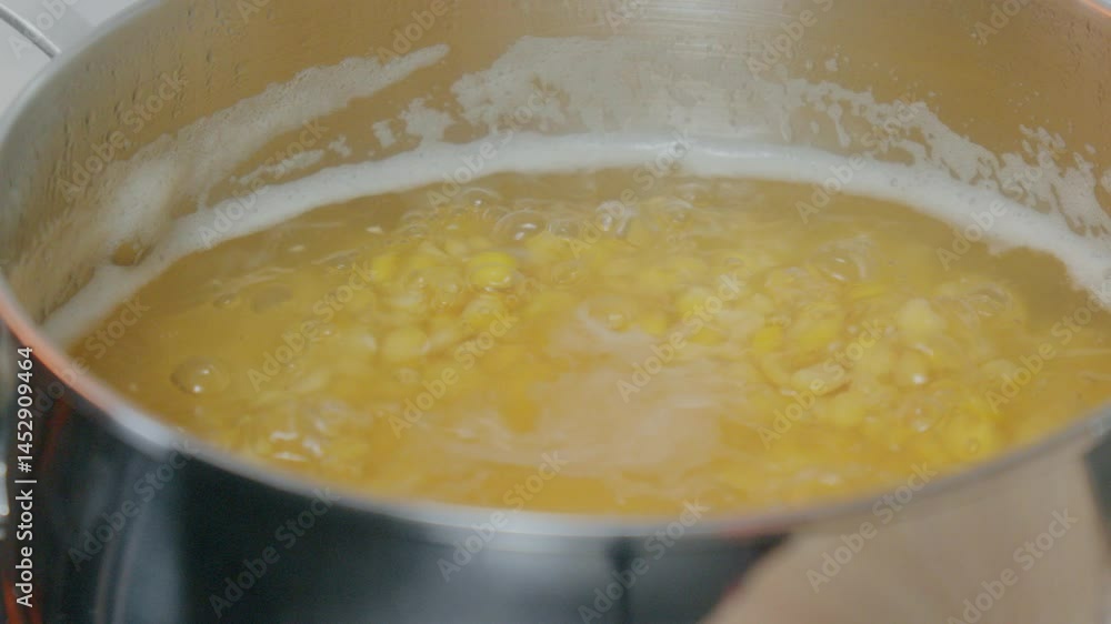A hand holds a spoon while stirring lentils simmering in a stainless steel pot on a sleek stovetop. A hand holds a spoon while stirring lentils simmering in a stainless steel pot on a sleek stovetop.