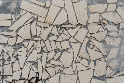 A wall with many pieces of broken tiles. The wall is white. The tiles are broken in different shapes and sizes.