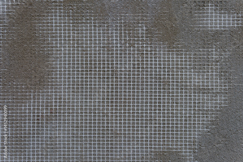 A grey wall with a white mesh pattern. The mesh is in the shape of squares.