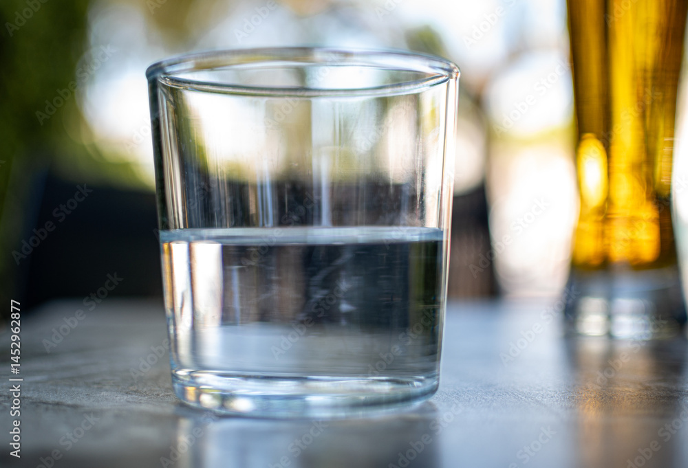 A half empty or a half full glass of water on a table with nice blurry background. A half empty or a half full glass of water on a table with nice blurry background.