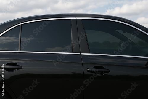 Side view of a sleek black car with dark tinted windows and chrome trim under a cloudy sky. Stylish automotive detail and privacy-focused design.