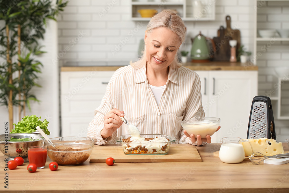 Beautiful mature happy woman cooking delicious lasagna at table in kitchen Beautiful mature happy woman cooking delicious lasagna at table in kitchen