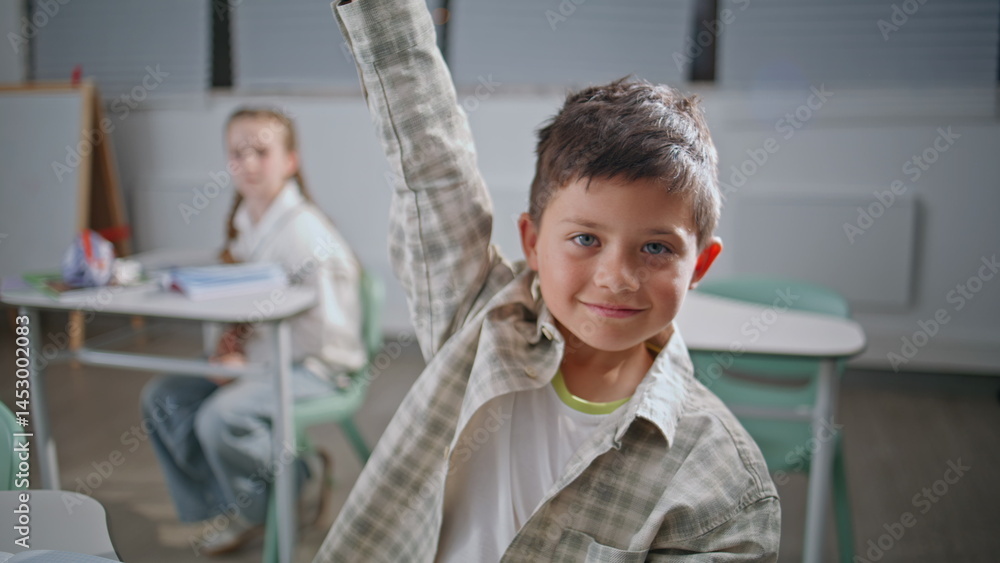 Fototapeta premium Portrait smart pupil studying at elementary school. Positive boy raising hand