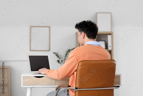 Young man working with laptop at table in office, back view