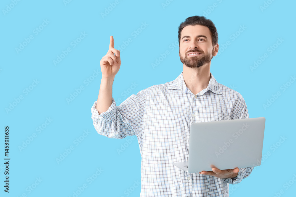 Handsome man with laptop pointing at something on blue background Handsome man with laptop pointing at something on blue background