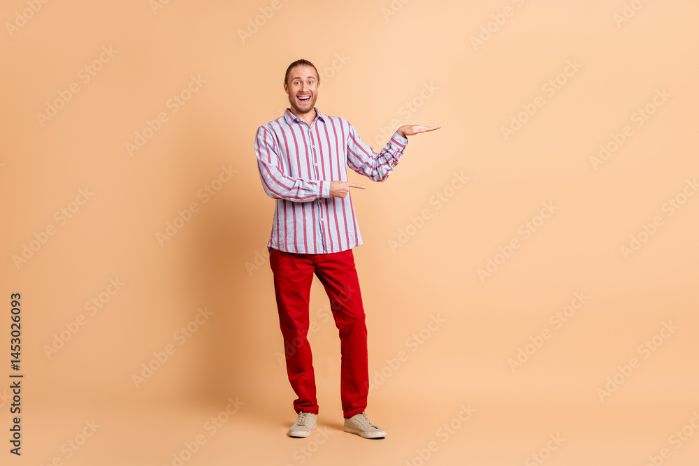 Confident Male Model with Casual Striped Shirt and Vibrant Red Pants Posing Against Beige Background Confident Male Model with Casual Striped Shirt and Vibrant Red Pants Posing Against Beige Background