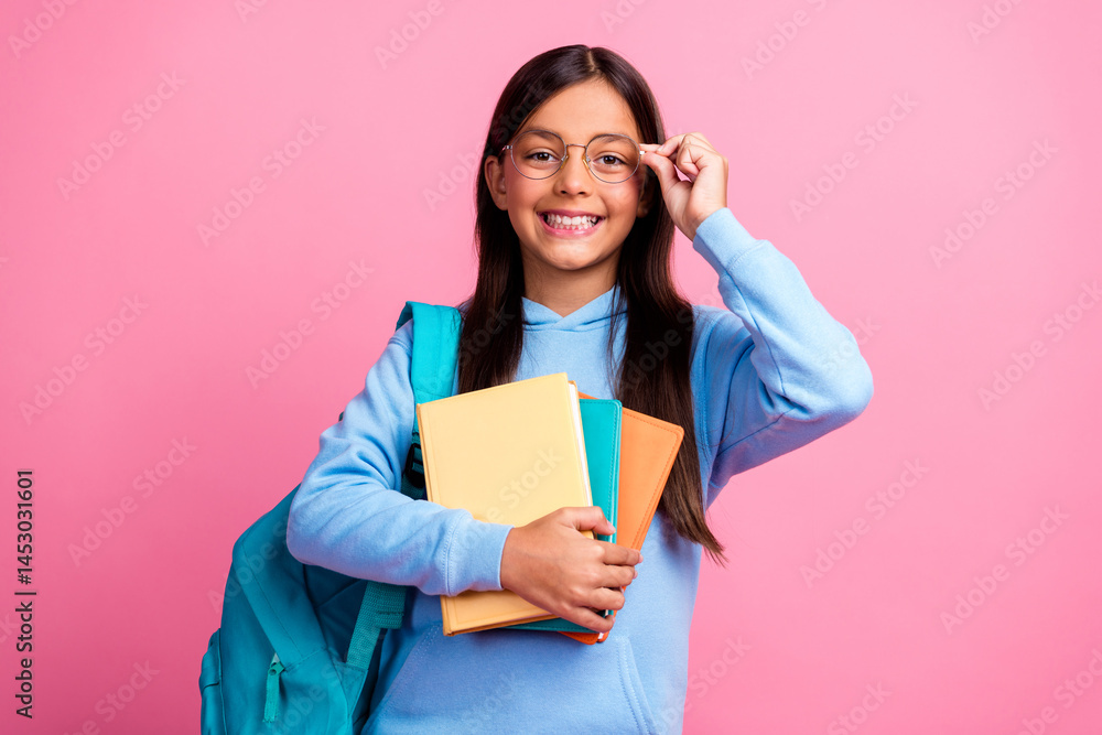 Happy young girl wearing glasses and holding colorful book dressed in a blue hoodie against a vibrant pink background Happy young girl wearing glasses and holding colorful book dressed in a blue hoodie against a vibrant pink background
