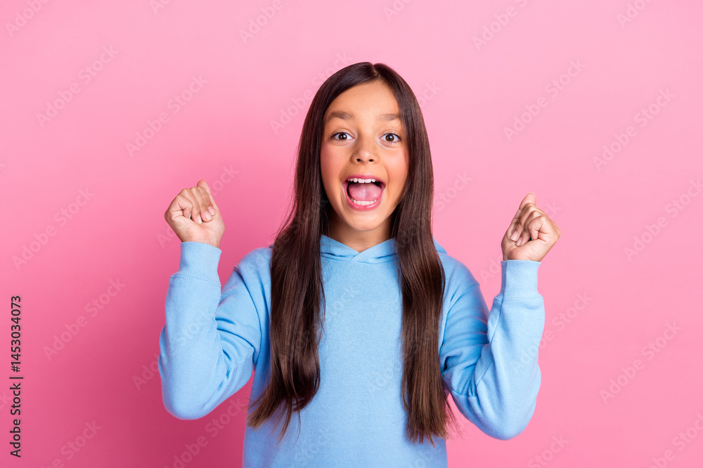 Excited preteen girl in blue sweatshirt making happy gestures against a vibrant pink background