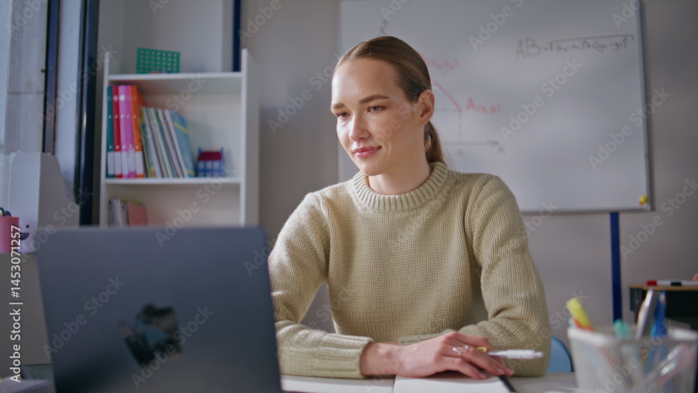 Smiling woman teaching online lesson using laptop sitting at class room closeup